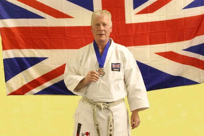 Sensei Fred Fawcett holding his european championship medal in front of a uk flag.